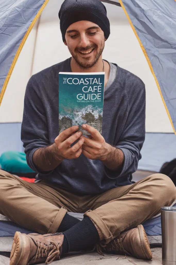 Man at campsite holding the Coastal Café Guide